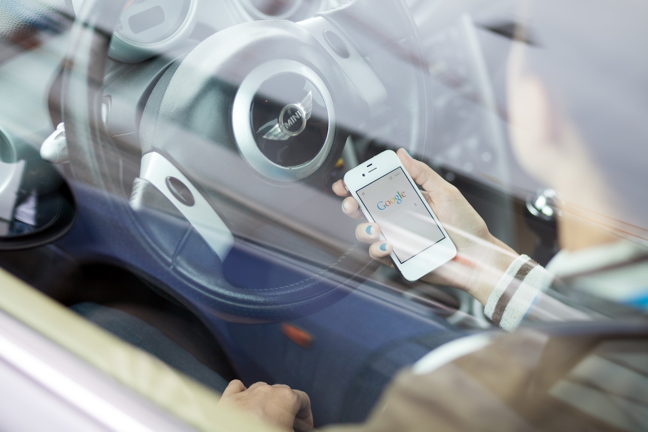 MINI App on a smartphone beside a MINI vehicle at MINI of Freeport in Freeport, New York