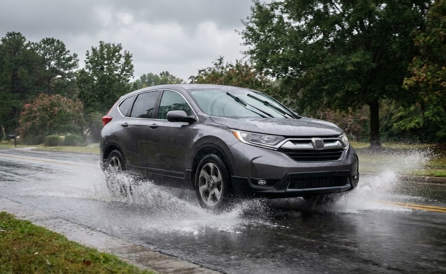 SUV driving through deep water on a rainy Georgia road, hydroplaning risk near Athens GA, wet leaves and red clay on pavement, fall storm driving hazard, Athens Ford Service Center tire safety tips, worn tire tread increasing stopping distance, Ford drivers navigating slick Atlanta Highway, fall and winter tire maintenance Athens Georgia, prevent sliding and loss of control on wet roads, local Ford dealership promoting tire inspections and replacement