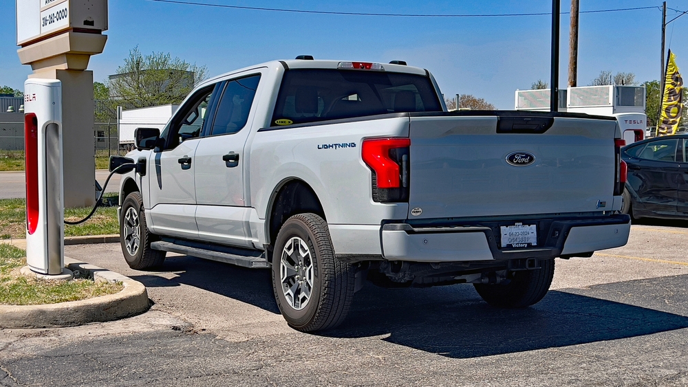 Ford F-150 Lightning charging at Tesla Supercharger, EV truck at public charger, electric pickup range New Hampshire, fast charging Ford EV truck, Tesla station Ford compatibility, Manchester NH electric vehicle travel, Ford Lightning on-road charging, long-range EV infrastructure image