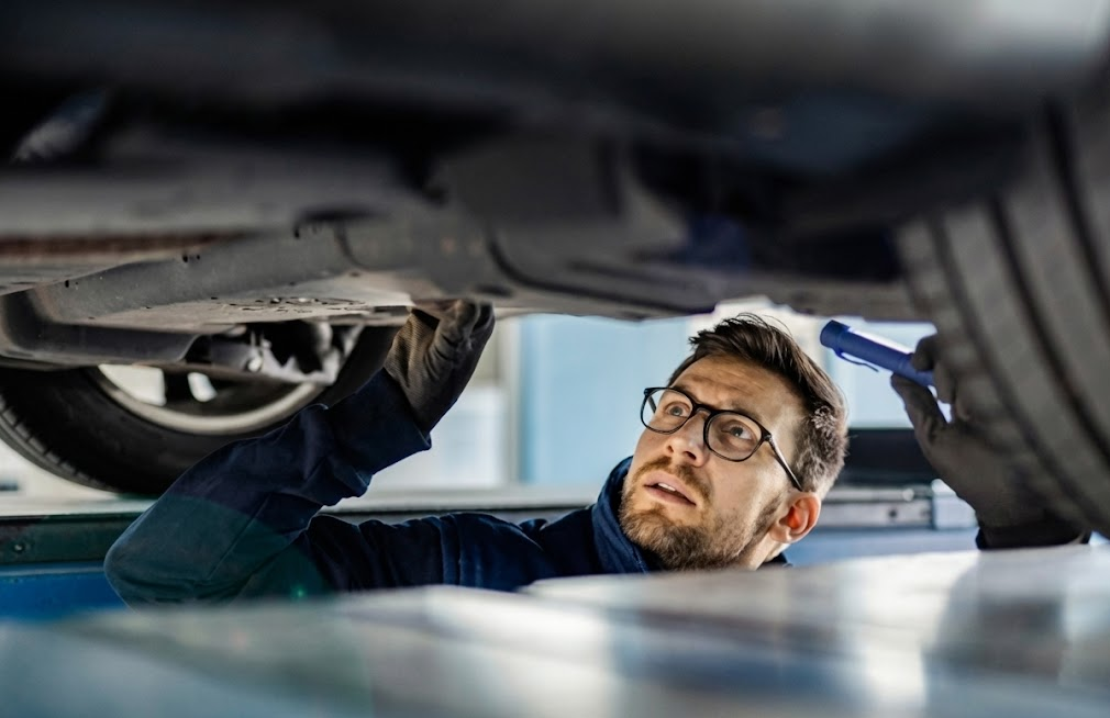 Hyundai certified technician inspecting underside of vehicle in service bay, mechanic checking suspension and exhaust with flashlight, professional multi-point inspection Alliance Hyundai North Fort Worth, preparing SUV for holiday travel, brake and tire safety check Fort Worth TX, factory trained Hyundai service expert, dealership maintenance before I-35 road trip, winter readiness inspection for North Texas drivers, comprehensive service and diagnostics at Hyundai dealer near Dallas and Denton