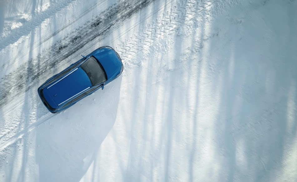 blue luxury sedan resembling BMW driving on snowy Long Island road, clear tire tracks in snow, winter highway travel near Freeport NY, BMW xDrive traction on icy lane, need for dedicated winter tires, safe lane control on frozen pavement, Nassau County winter road scene, BMW winter maintenance reminder, cold weather driving example from BMW of Freeport Service Center