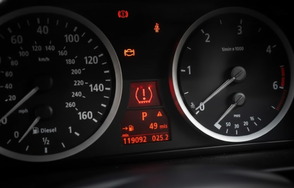 Close up of BMW dashboard gauges with warning lights illuminated, battery system alert, electrical fault icon, start stop system warning, BMW battery management problem, Freeport NY driver seeing red and amber dash lights, signs of failing BMW battery and IBS sensor issues, need for DME battery registration at BMW of Freeport Service Center, Long Island high tech BMW instrument cluster