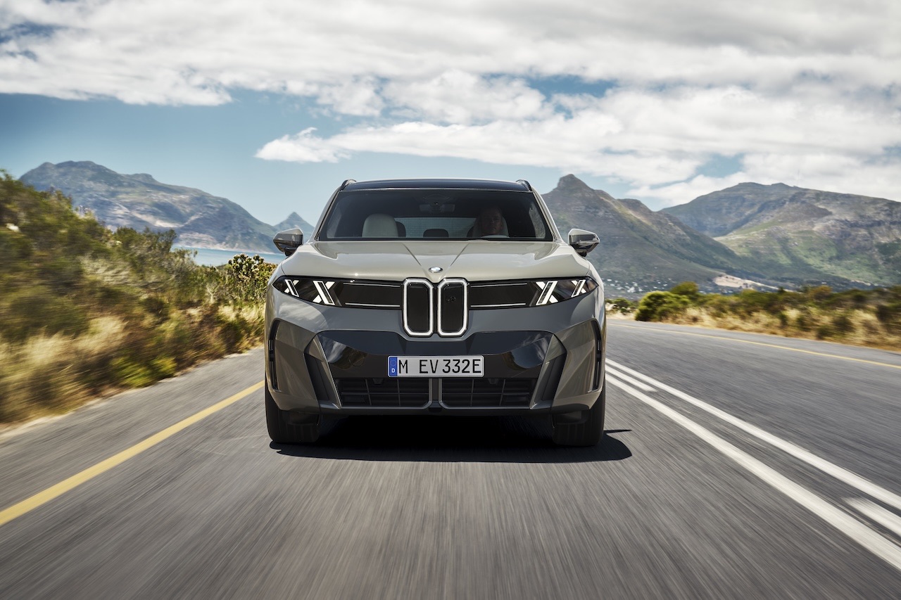 2027 BMW X5 driving along a coastal road, front three-quarter view
