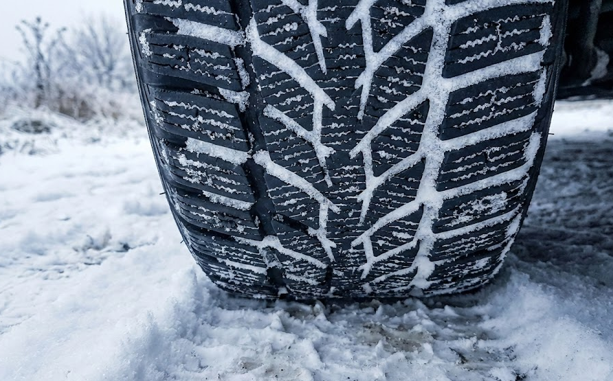 Closeup of winter tire tread packed with snow, deep grooves and sipes designed for icy Colorado roads, three-peak mountain snowflake winter tire symbol performance, cold weather rubber compound staying soft below 45 degrees, snow-covered ground in Colorado Springs, example of dedicated snow tires versus all-season tires, winter traction and stopping power for Nissan SUVs and sedans, Woodmen Nissan Service winter tire installation, Colorado driver preparing vehicle for Code 15 traction law season