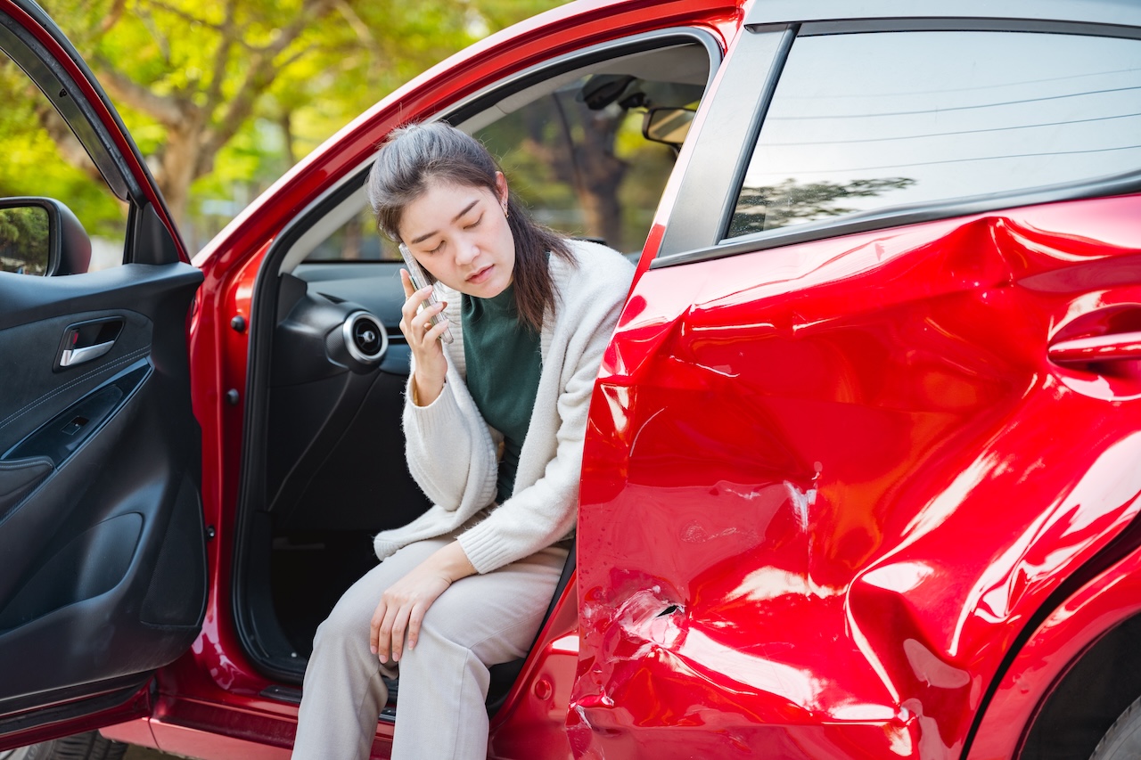 Car owner standing next to a vehicle with a dented door calling their insurance company after an accident near a collision repair center offering ADAS calibration services in Manchester, NH