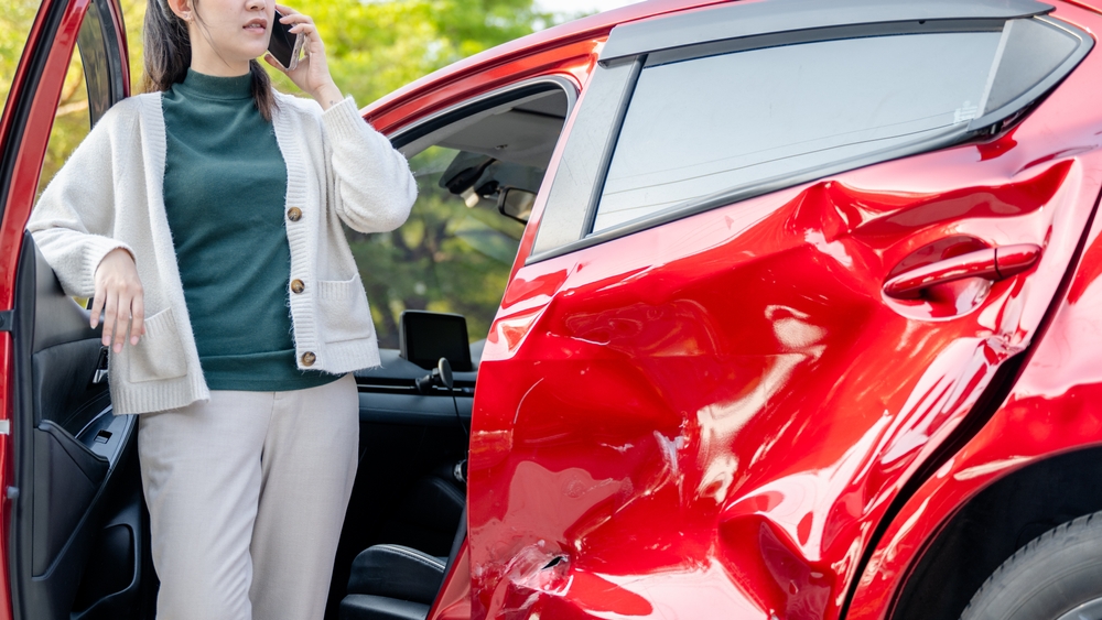 damaged red SUV Naples FL, post-collision insurance call, car accident ADAS recalibration Naples, dented vehicle rear door, luxury SUV damage, collision repair Naples, Naples Premium Collision Center, car crash scene Southwest Florida