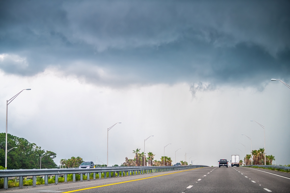 Daytona Beach storm clouds over Florida highway, summer rainy season squall line, Mazda i-ACTIV AWD predictive traction, AWD service near Daytona, prepare for A1A and I-95 downpours, hydroplaning prevention, Daytona Mazda Service experts, AWD inspection and maintenance, coastal weather driving safety, wet pavement braking and stability control