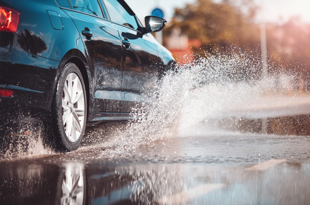 Car splashing through rain puddle, wet road hydroplaning risk, Mercedes tire traction Florida storms, hurricane rain driving tips, tire pressure check Daytona, safe driving I-95, Florida downpour visibility, Mercedes service Daytona Beach tire inspection, wiper blades and tread depth
