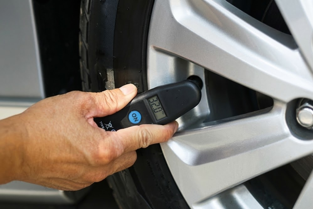 hand using digital tire pressure gauge on Nissan wheel valve stem, accurate PSI reading for TPMS tire maintenance, professional tire pressure check at Ted Russell Nissan Service Center Knoxville TN, close up of aluminum alloy wheel and tire, checking and adjusting air pressure during cold weather, complimentary tire fill and inspection, Nissan service technician tools, proper tire inflation for fuel economy and safety, East Tennessee fall and winter tire care, Nissan Express Service tire check near Kingston Pike