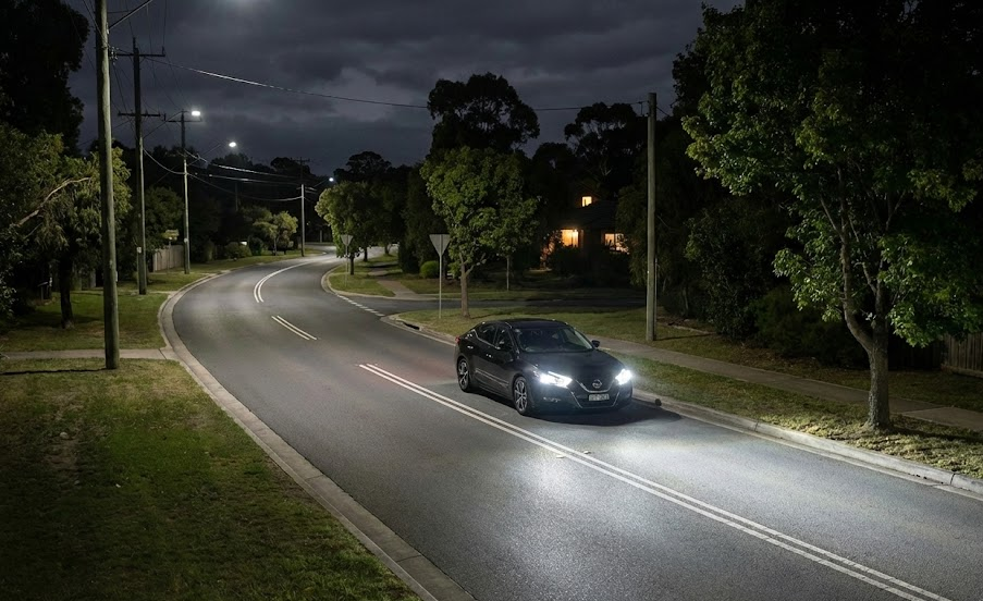 modern Nissan sedan driving at night with bright LED headlights, powerful beam lighting Charlotte neighborhood street, improved visibility after headlight restoration or genuine Nissan assembly replacement, safe night driving during North Carolina deer season, Independence Boulevard style roadway, East Charlotte Nissan Service safety upgrade, Top Safety Pick style illumination