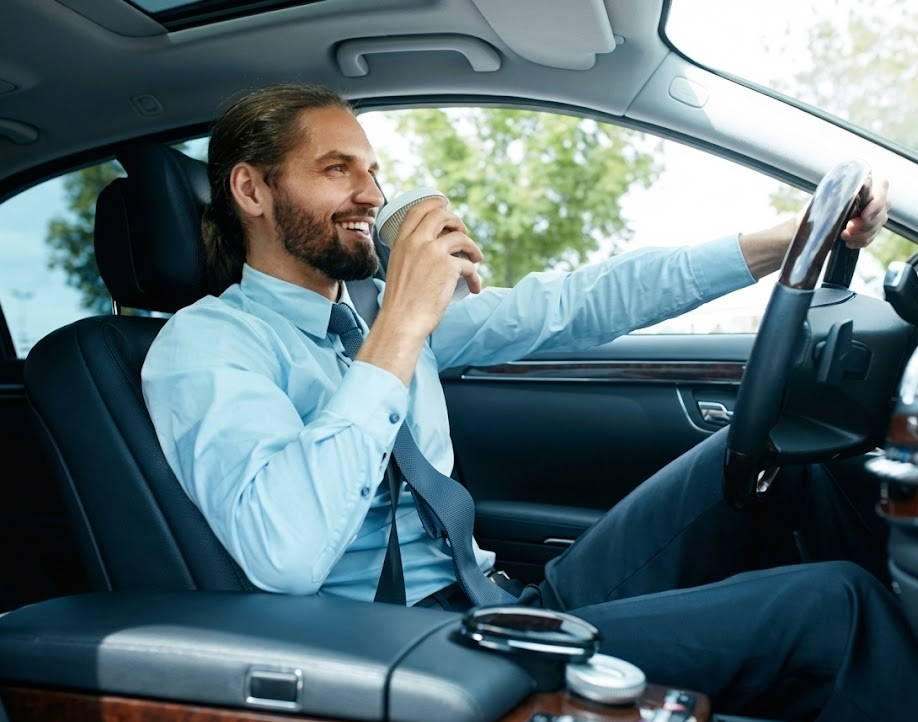 smiling driver enjoying morning commute in comfortable car, relaxed after Nissan TPMS light is reset, East Charlotte Nissan Service happy customer, Charlotte NC professional driving to work with coffee, confident knowing tire pressure is correct, stress free winter driving after complimentary tire check, safe Nissan maintenance near Independence Blvd, Charlotte driver pleased with Express Service experience, worry free highway driving in serviced Nissan sedan