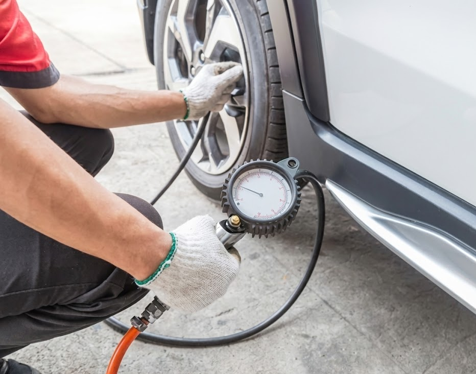 auto technician in gloves checking tire pressure with digital gauge, filling air in tire at East Charlotte Nissan Service, complimentary tire pressure check Charlotte NC, professional TPMS diagnosis for Nissan vehicles, winter tire PSI adjustment near Independence Blvd, closeup of tire pressure gauge and valve stem, Nissan maintenance and safety inspection, factory-trained technician servicing Nissan Rogue and Altima, Charlotte driver getting quick Express Service tire fill