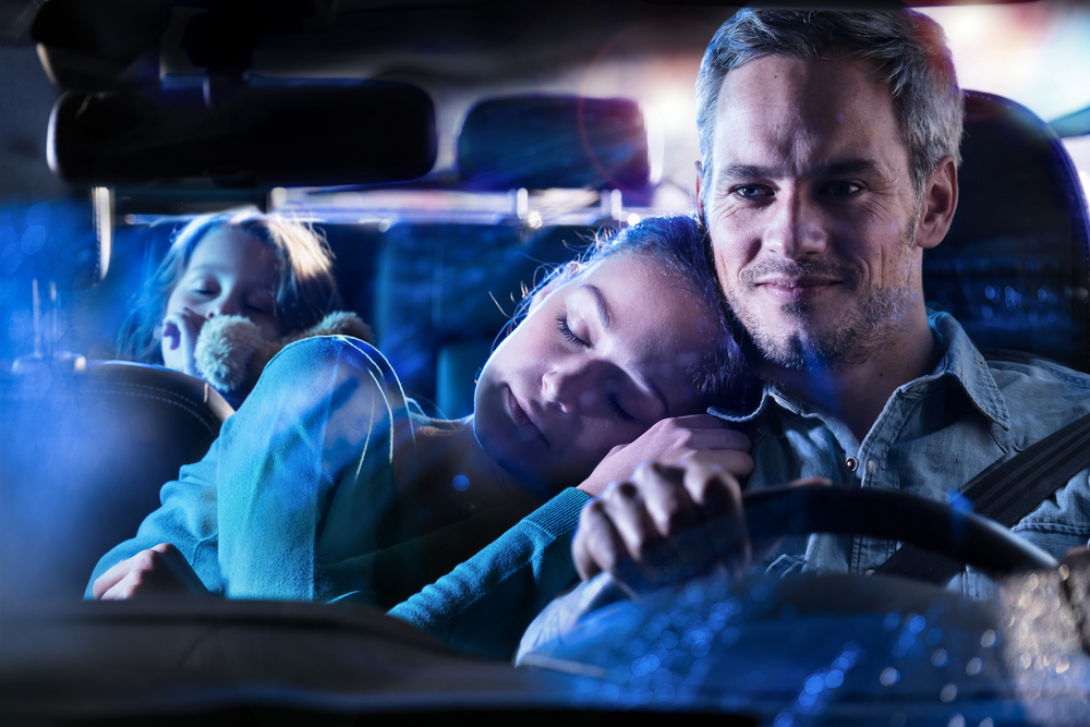 A father drives his family safely in their Nissan during a nighttime hurricane evacuation, showing the importance of pre-storm vehicle prep from Naples Nissan Service Center in Naples, FL.