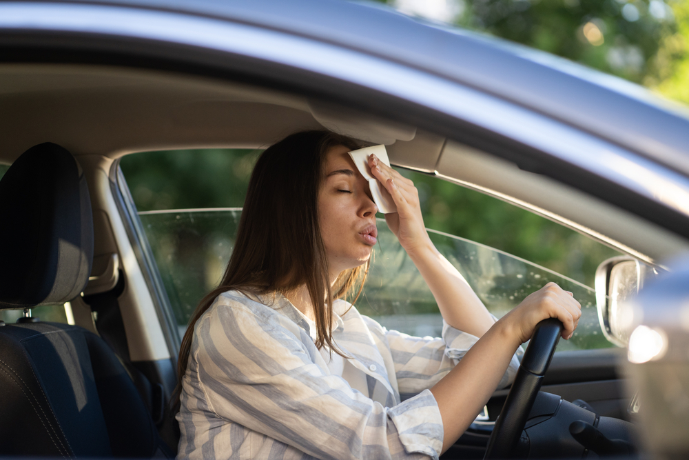 female driver sweating in hot car, Gainesville Florida summer heat, car A/C failure, Nissan air conditioning problem, North Central Florida auto repair, hot car symptoms, why A/C recharge matters, Gainesville Nissan service