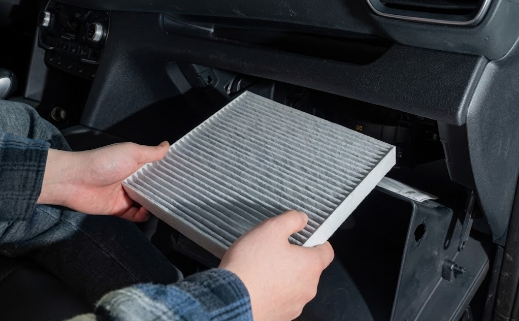 Service technician installing clean new cabin air filter behind glove box, professional Hyundai cabin air filter replacement at Alliance Hyundai Service Fort Worth TX, genuine Hyundai parts for Palisade Tucson Santa Fe and Elantra, improve HVAC airflow and odor control, protect sensitive electronics and AC system, scheduled maintenance for North Texas allergy season