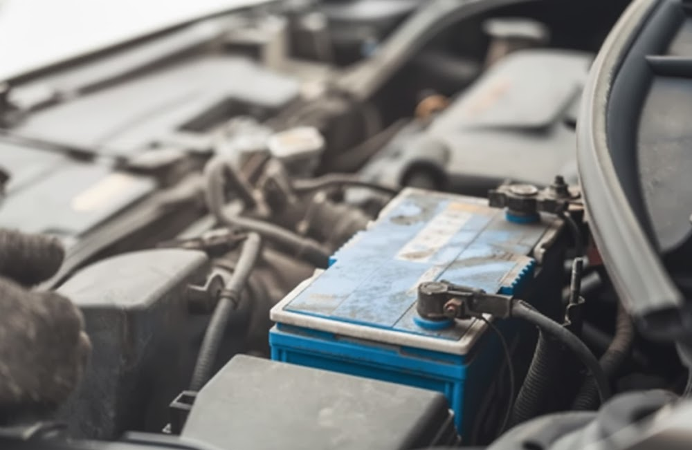 auto technician inspecting worn car battery in cold weather, weak battery under hood of INFINITI crossover, rear window defroster drawing high electrical load, Lake Norman INFINITI winter battery test Cornelius NC, comprehensive battery health check and charging system diagnostic, prevent no start on cold morning, ensure strong power for front and rear defrosters, INFINITI battery replacement specials near Lake Norman Davidson Huntersville