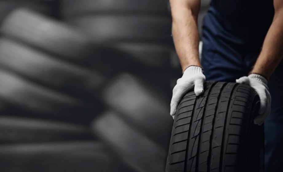 Certified technician in uniform and gloves rolling tire for inspection, Mercedes-Benz of Massapequa Service Center, tire wear check and 4-wheel alignment, uneven tread wear from misalignment, Long Island NY Mercedes-Benz maintenance, factory trained technicians using precision equipment, fall pre-winter service for 4MATIC SUVs and sedans, Nassau County alignment and tire rotation specials