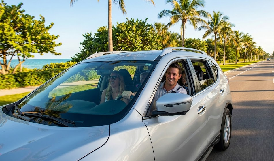 Smiling family driving silver Nissan SUV along Naples Florida palm-lined road, happy snowbirds enjoying Gulf Coast vacation after service, Rogue or Murano cruising near Vanderbilt Beach, safe reliable Nissan after post-storage inspection, Naples Nissan Service Center customer satisfaction, stress-free seasonal driving in Southwest Florida, family road trip on sunny day, Naples FL dealership service and maintenance, confident driving after battery tire and fluid check