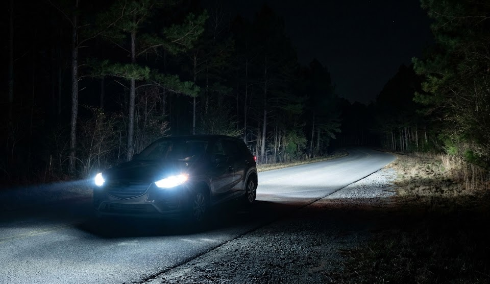 SUV with bright LED headlights on dark wooded Georgia road, modern headlight technology lighting up rural highway, nighttime driving near Athens GA, LED headlight upgrade for Nissan drivers, wide beam pattern for deer detection, Nissan of Athens Service visibility improvement, safe driving during November rut season, headlights illuminating forest tree line, high beam assist style lighting, Athens area backroad safety at night