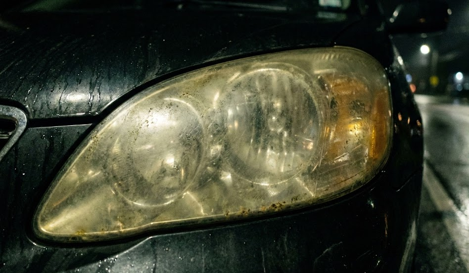 close up of yellow cloudy oxidized car headlight lens, foggy plastic headlight housing, worn polycarbonate headlights on older sedan, poor nighttime visibility from dirty headlights, headlight restoration before and after concept, Tennessee UV damage to Nissan headlights, Cookeville TN vehicle maintenance, cloudy headlight problem image, need professional headlight restoration Nissan of Cookeville