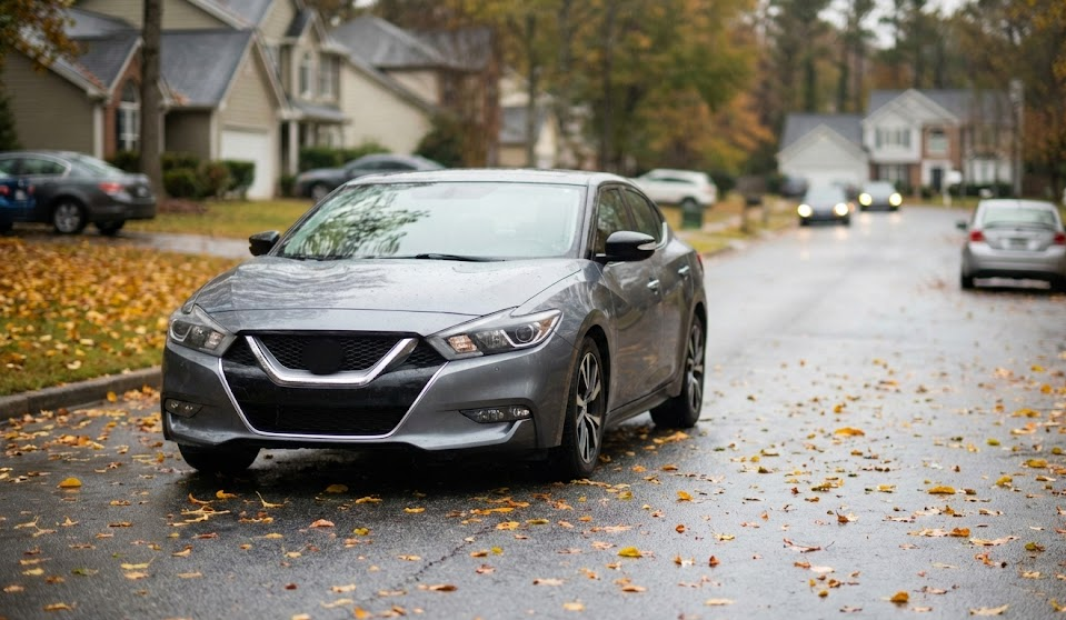 Nissan sedan driving on wet fall leaves in neighborhood street, McDonough Nissan wheel alignment blog, fall driving safety Henry County GA, slippery leaf-covered road near Jonesboro Road McDonough, Nissan pulling on wet pavement, autumn weather tire traction issues, Georgia rainy season road hazards, Nissan service center near Eagles Landing Parkway, local Nissan dealer in McDonough Georgia, alignment check for drifting steering wheel, prepare your Nissan for fall weather in Henry County