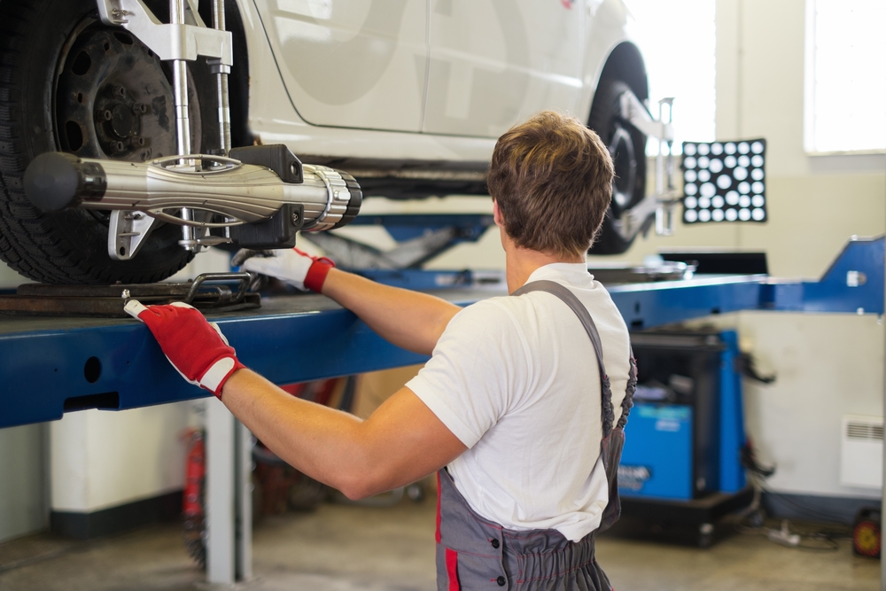 Nissan wheel alignment service Charlotte NC, Scott Clark Nissan certified technician adjusting wheel alignment, professional tire alignment machine on Nissan car, precise wheel alignment for better handling, Charlotte Nissan dealership service center, Nissan suspension and steering adjustment, accurate alignment for safe driving, expert Nissan maintenance Charlotte North Carolina, vehicle on lift during wheel alignment service, Nissan alignment technician using advanced tools