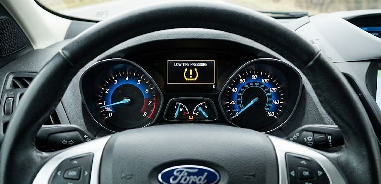 Ford steering wheel and instrument cluster, low tire pressure TPMS warning light on dashboard, Ford sedan interior low tire pressure alert, cold weather tire pressure drop in Palm Bay FL, Ford TPMS system explaining Florida cold front effect, Brevard County driving safety, Palm Bay Ford Service reminder to check PSI, Ford tire inspection and nitrogen fill services