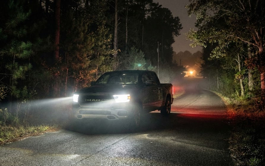 Ram pickup truck driving on dark rural Georgia road at night, bright headlights cutting through fog, Coweta County backroad near woods, Ram prepared for deer season with aligned headlights and Mopar brakes, nighttime driving during November rut, Newnan Chrysler Dodge Jeep Ram safety preparation, Ram 1500 on narrow country lane, avoiding deer collisions with proper visibility, rural Newnan GA evening scene