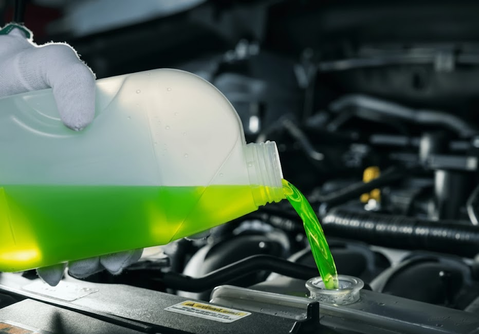 Mechanic pouring bright green engine coolant into radiator, cooling system flush with fresh antifreeze, Nissan coolant service Charlotte NC, Genuine Nissan Long Life Coolant change, prevent rust and sludge buildup, protect aluminum heater core and radiator, prepare Nissan Rogue Altima Pathfinder for winter, pre-winter coolant service at Scott Clark Nissan Service on South Boulevard, coolant flush to restore heat and prevent overheating