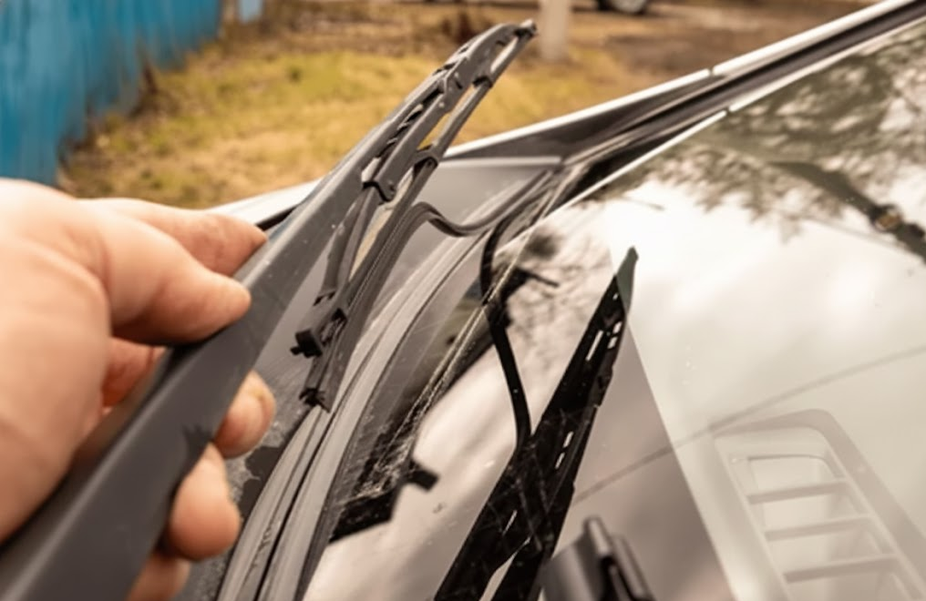 mechanic hand changing windshield wiper blade, close up of worn rubber on car windshield, Nissan wiper replacement at Scott Clark Nissan Service, Charlotte NC fall rain preparation, genuine Nissan wiper blades installation, streak-free windshield for I-77 driving, UV damaged wiper rubber from Piedmont summers, visibility maintenance before Charlotte thunderstorms, auto service technician replacing front wiper, Nissan visibility service specials