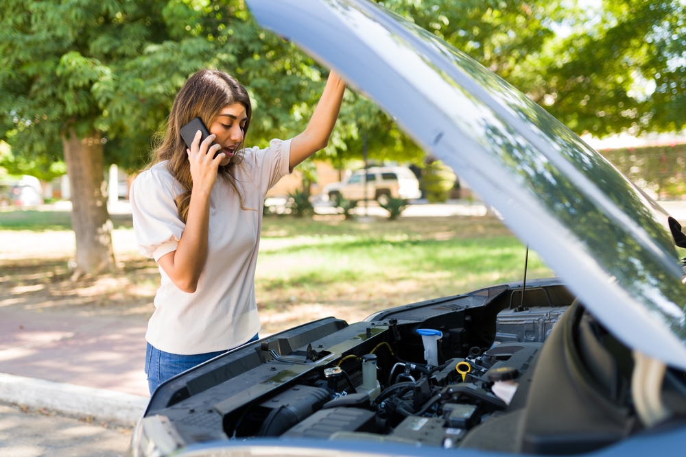 woman calling roadside assistance for dead car battery, stranded Nissan driver Knoxville TN, Nissan battery failure symptoms, Smoky Mountains trip car breakdown, dead car battery in fall, Knoxville Nissan battery emergency, East Tennessee road trip prep