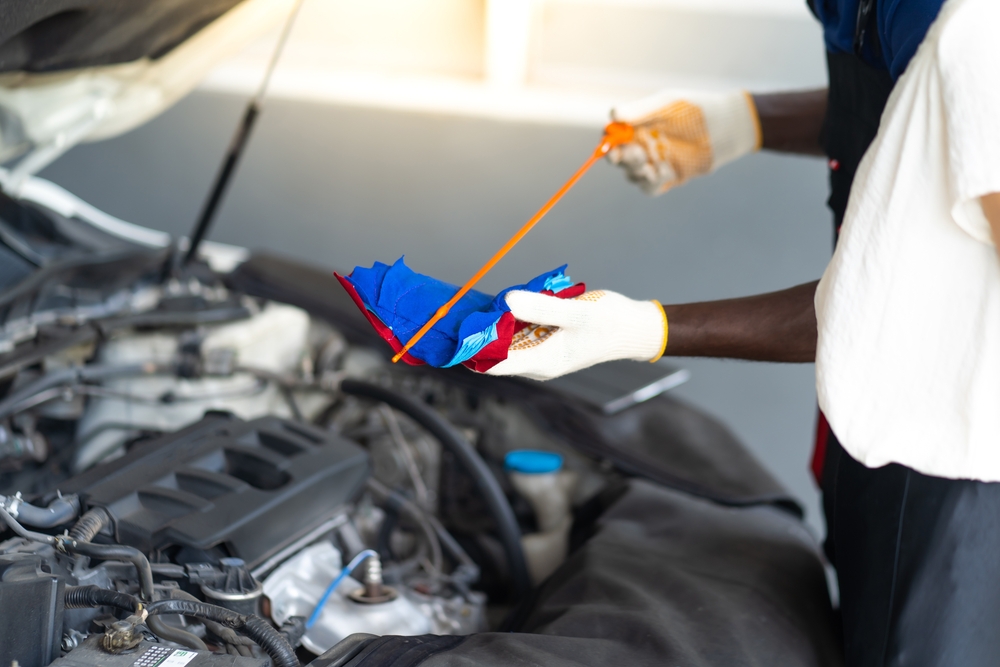 Professional Nissan mechanic checking oil dipstick in Knoxville service center, genuine Nissan parts and fluids, factory-trained technician performing summer oil change, expert Nissan maintenance Tennessee, prevent engine damage from heat, Ted Russell Nissan trusted service team, oil quality inspection Knoxville TN