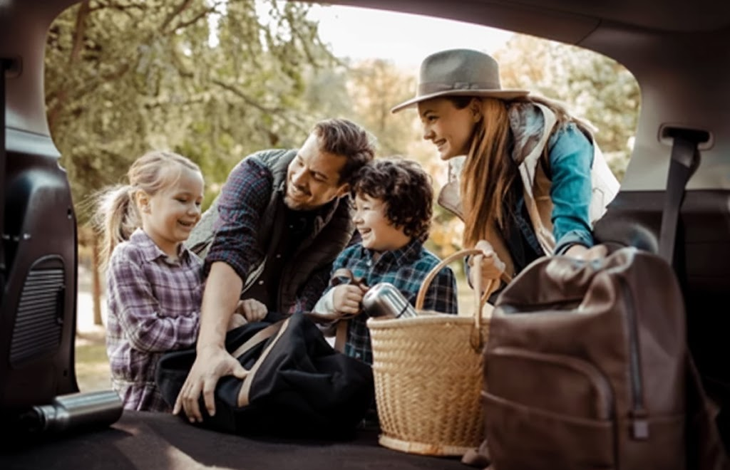 happy family packing SUV for Thanksgiving road trip, parents and kids loading bags and picnic basket into crossover, Stone Mountain Volkswagen family travel, VW style SUV ready for holiday drive, aligned and balanced tires for safe Georgia highways, fall foliage in background, stress free VW road trip from Stone Mountain to North Georgia or Savannah, Volkswagen service complete before vacation, safe reliable family vacation vehicle near Atlanta