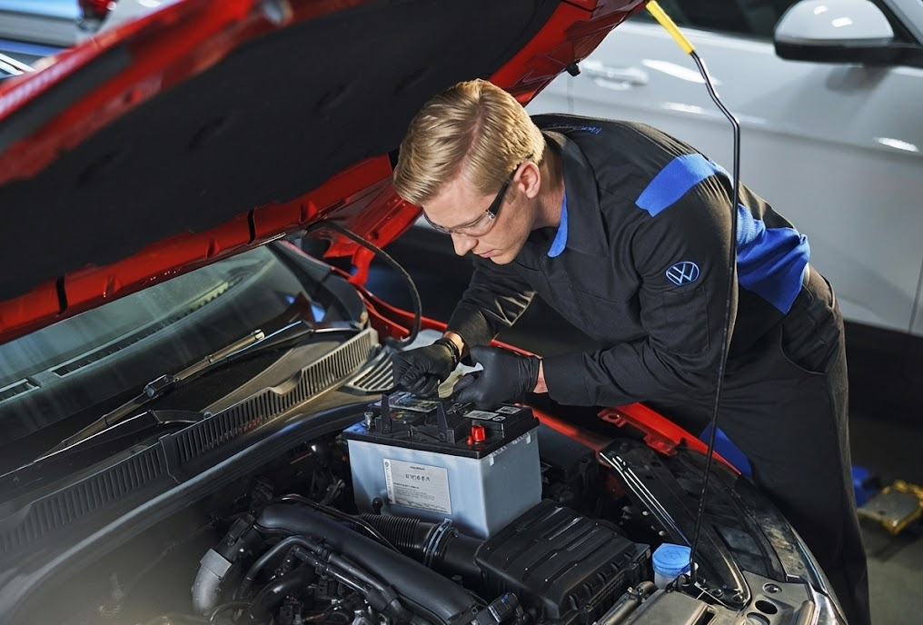 Certified Volkswagen technician testing and replacing car battery under hood, VW service expert using diagnostic tools, Stone Mountain Volkswagen Service Center in Snellville GA, factory trained mechanic performing battery inspection, VW battery management system programming and registration, professional dealership level auto repair, Atlanta area VW battery replacement specials, genuine Volkswagen parts and electrical system care, trusted local VW service team